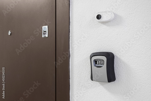 Key box with a combination lock next to the door and a bell button on the wall photo
