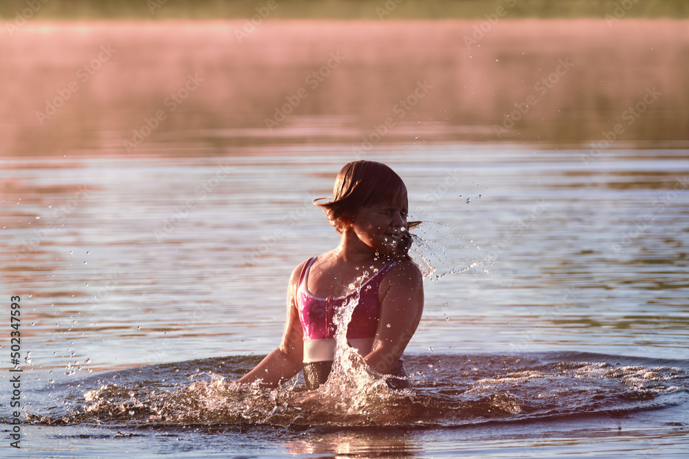 Fototapeta premium A happy child is bathing in the water . The girl splashes water in the river . Happy childhood . Children 's summer holidays . Outdoor play
