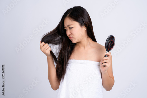 Stressed young Asian woman holding damaged dry hair on hands over white isolated background.