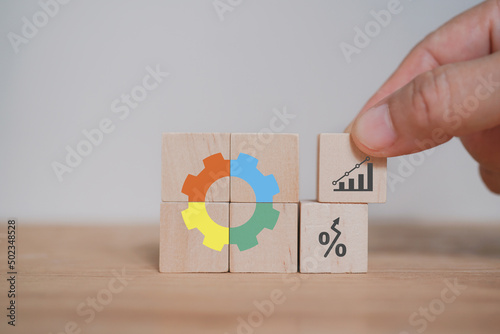 Businessman's hand arranged wooden cube blocks with multi color of gear icon included copy space on orange background, for key to success and team work concept