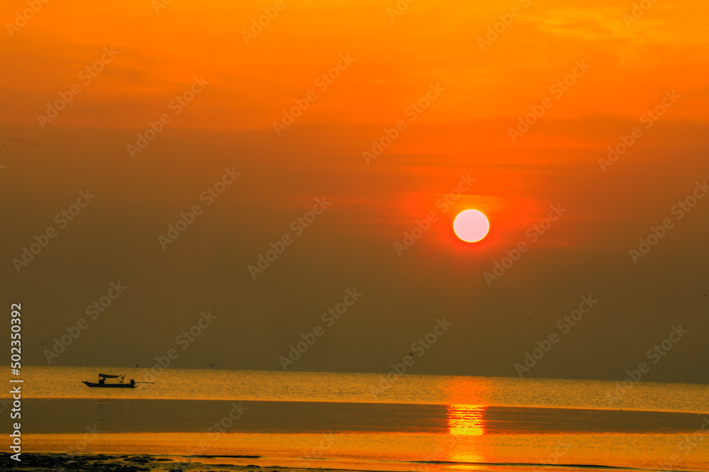 Blurred nature background of the morning sun by the sea, a beautiful golden light, among the trees, rocks and local fishing boats, the beauty of nature during the day.