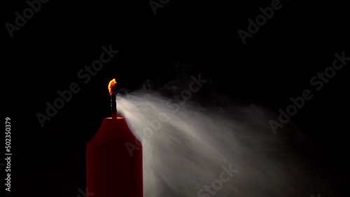 A red candle flame burns in the darkness, slow motion, then is blown out.