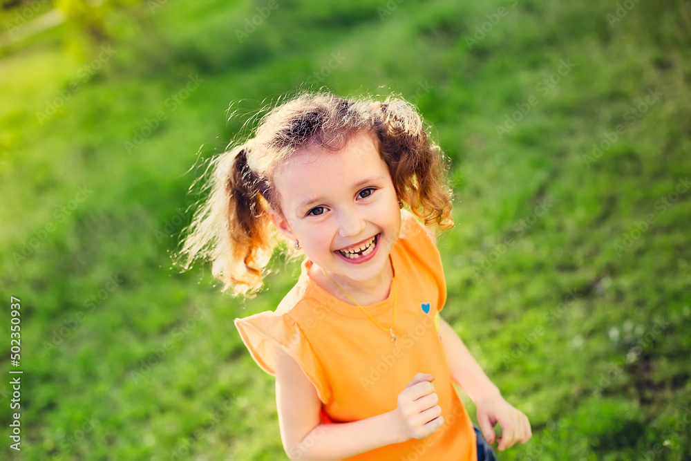 The little girl laughs. Girl running on green grass in the spring.The child's teeth fall out. Girl with two tails on the head. Soft focus The little girl laughs. Girl running on green grass in the spring.The child's teeth fall out. Girl with two tails on the head. Soft focus