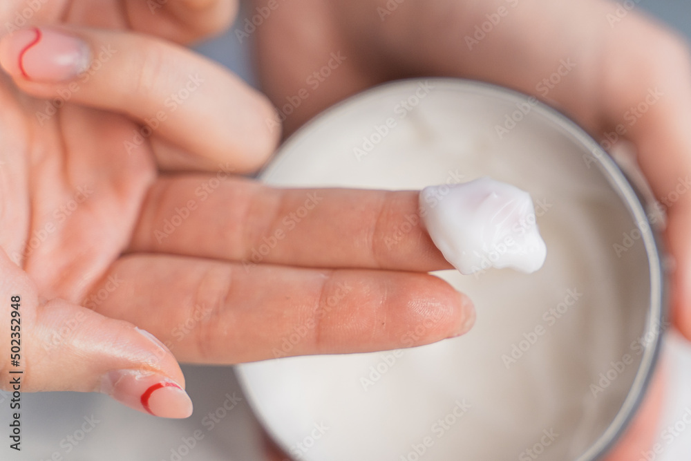 Naklejka premium the girl takes out white cream from the jar with her fingers close-up