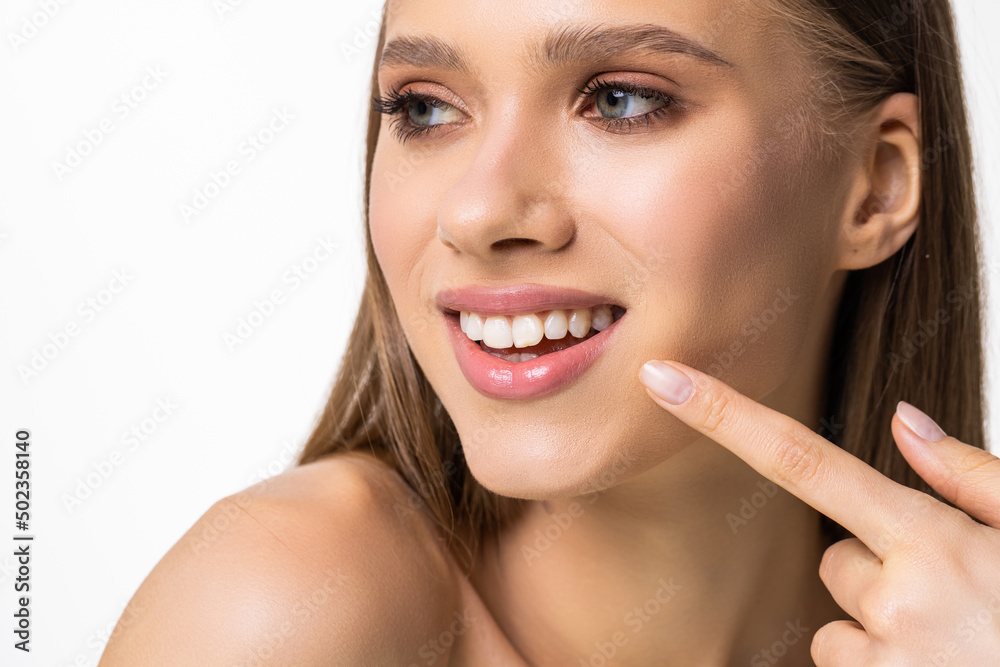 Young beautiful woman with perfect skin, bright spring pink make-up and naked shoulders on a white background. Cheerfully smiles. Pointing fingers at snow-white teeth. Young beautiful woman with perfect skin, bright spring pink make-up and naked shoulders on a white background. Cheerfully smiles. Pointing fingers at snow-white teeth.