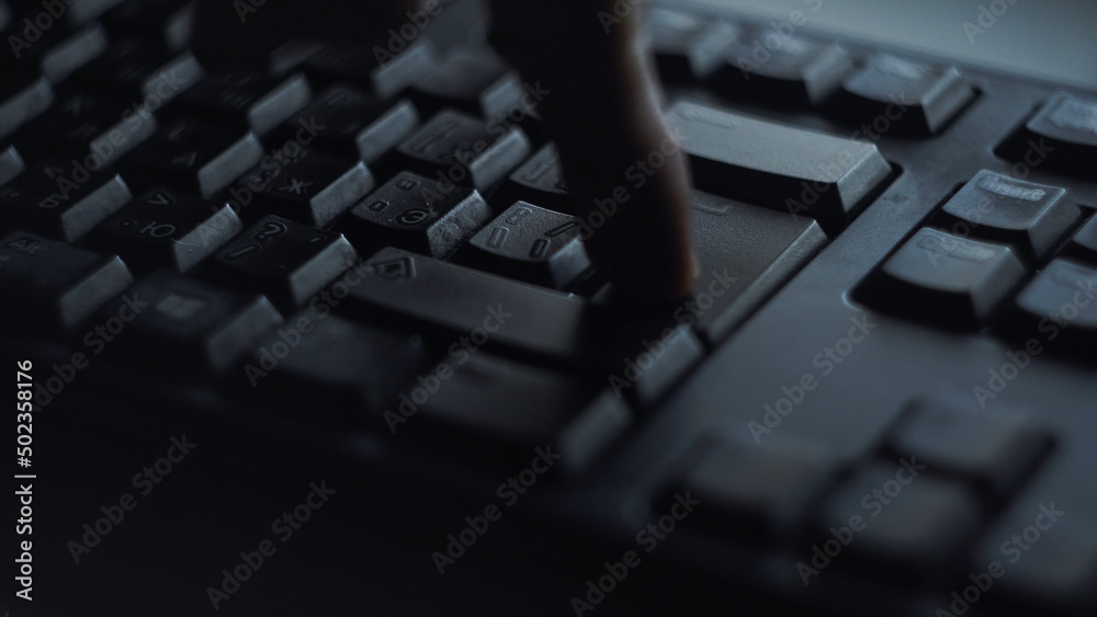 Close-up man presses keyboard key. Man presses button enter computer keyboard. Man's hand presses keyboard in light of computer screen