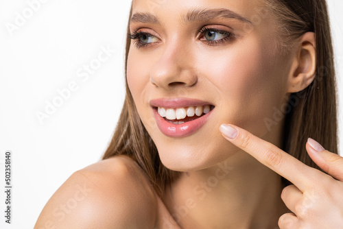 Young beautiful woman with perfect skin  bright spring pink make-up and naked shoulders on a white background. Cheerfully smiles. Pointing fingers at snow-white teeth.