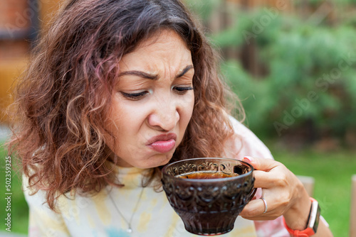 The girl tastes bitter and strong pu-erh tea or coffee and makes a disgruntled face. photo