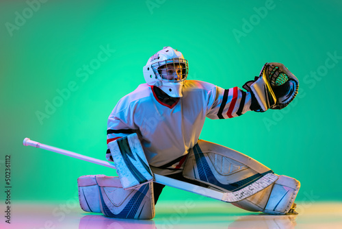 Photography Dynamic portrait of boy, hockey player, goalkeeper catching puck with special glove isolated on green background in neon light