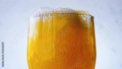 Orange soda is pouring into a glass with ice cube close-up on a white wall background. Overflowing wet glass with pop orange soda. 4k macro raw video with speed ramp effect.
