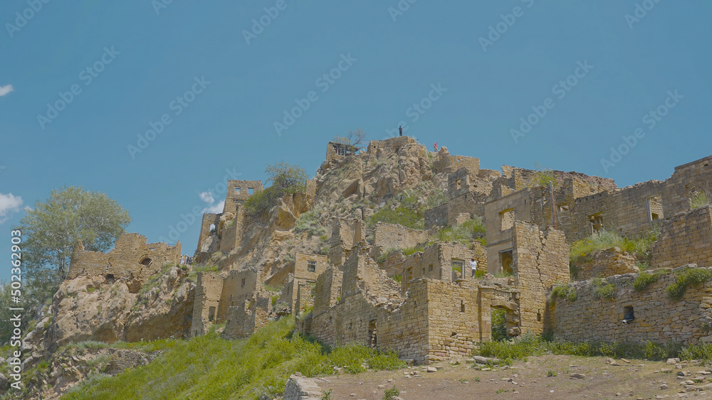 Tourists in abandoned stone city in mountains. Action. Beautiful ruins of stone city in mountains on sunny day. Tourists on ruins of ancient city made of stones
