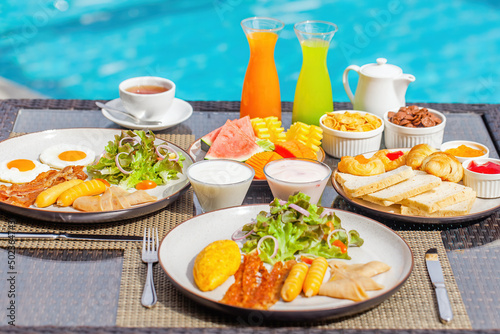 Breakfast in hotel. Woman hand take a piece of watermelon on breakfast on table with beautiful tropical view of blue pool. Morning food on summer romantic vacation. Luxury travel and lifestyle
