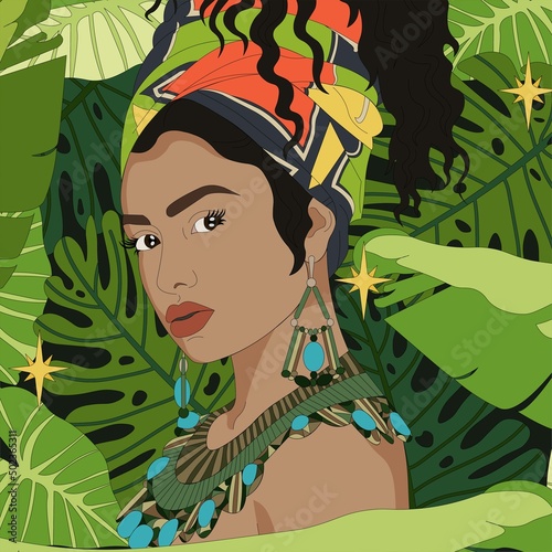Portrait of African American woman in ethnic headscarf and jewelry. Woman on a background of tropical plants.