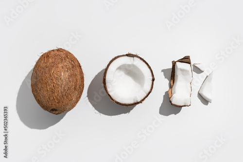 Fresh whole and broken pieces tropical coconut nut with sunny contrast shadows on light gray background flat lay top view. Creative summer food background, exotic organic healthy diet fruit