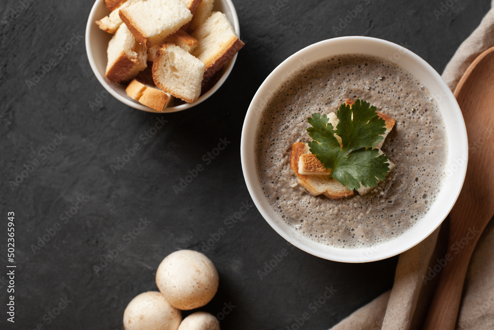 Bowl of homemade champignon mushrooms cream soup with croutons and parsley on concrete table.