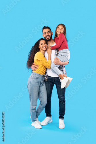 Arabic Man Hugging Wife And Holding Daughter On Blue Background