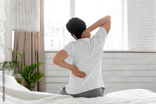 Unrecognizable man suffering from back pain at home in bedroom photo