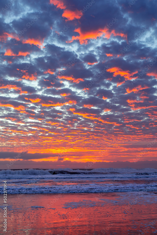Fototapeta premium Colourful golden cloudy skies at sunrise, viewed from the beach