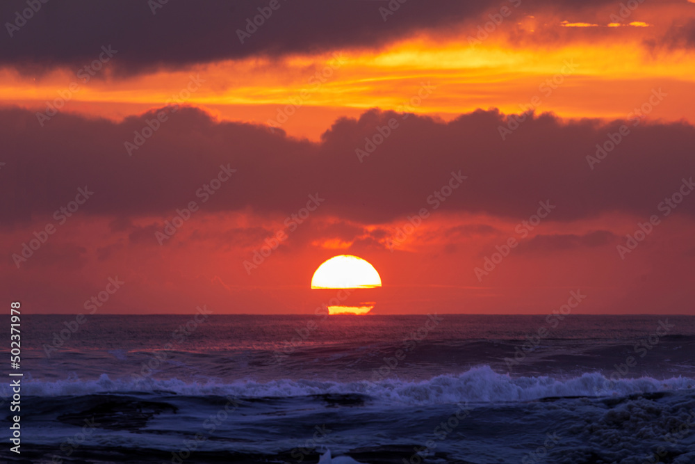 Orange cloudy skies at sunrise as the sun rises over the ocean