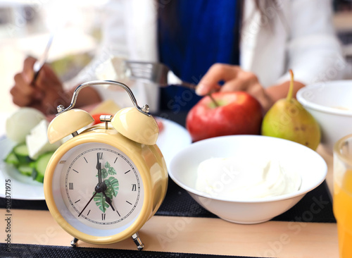 Selective focus of yellow alarm clock Intermittent fasting eight hour feeding window concept with woman eating a healthy food background
