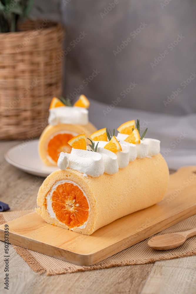 Orange roll cake topping with fresh cream orange and rosemary paste on wooden board.
