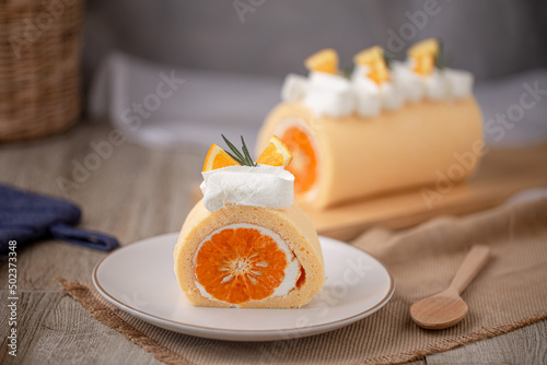 Orange roll cake topping with fresh cream orange and rosemary paste on white plate.