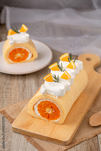 Orange roll cake topping with fresh cream orange and rosemary paste on wooden board, top view.