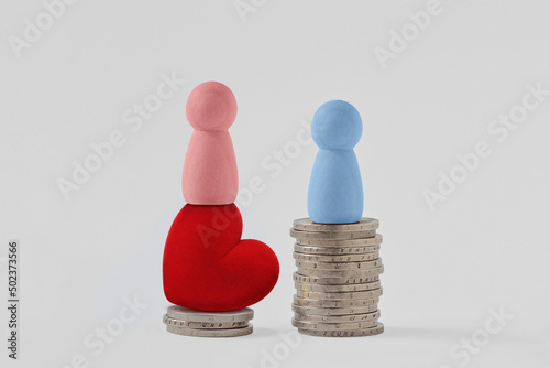 Pink pawns with heart and blue pawn on piles of coins - Concept of woman power and gender pay gap photo