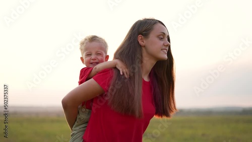 Family in piggyback park. Peace and harmony. Holiday in park on the grass. Mom and baby have fun in park. People play in the park. son smiles at mom. Family joys of mother and baby. Picnic in nature