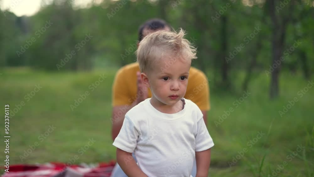 Happy family in the park. The father teaches the child. Baby's first steps. Family game in the park. The kid takes the first steps on the green grass. Father and son play on green grass in the park Happy family in the park. The father teaches the child. Baby's first steps. Family game in the park. The kid takes the first steps on the green grass. Father and son play on green grass in the park
