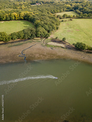 Aerial view of the River Hamble as a speed boat creates a wake in the water and passes woodland scene, Hamble, Southampton, United Kingdom. photo