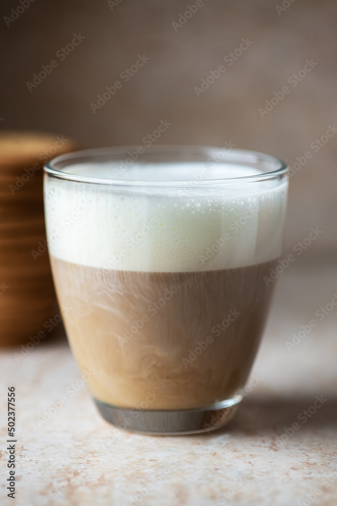 Hot coffee with milk foam in a transparent glass. Close up.