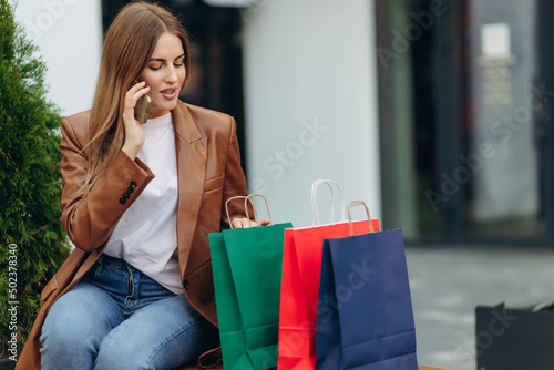 Young woman on the street with colored bags talking on a cell phone