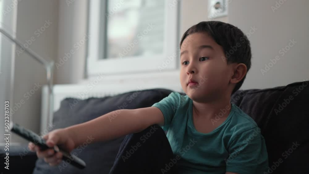 Little cute boy switch channels with remote control on TV at home
