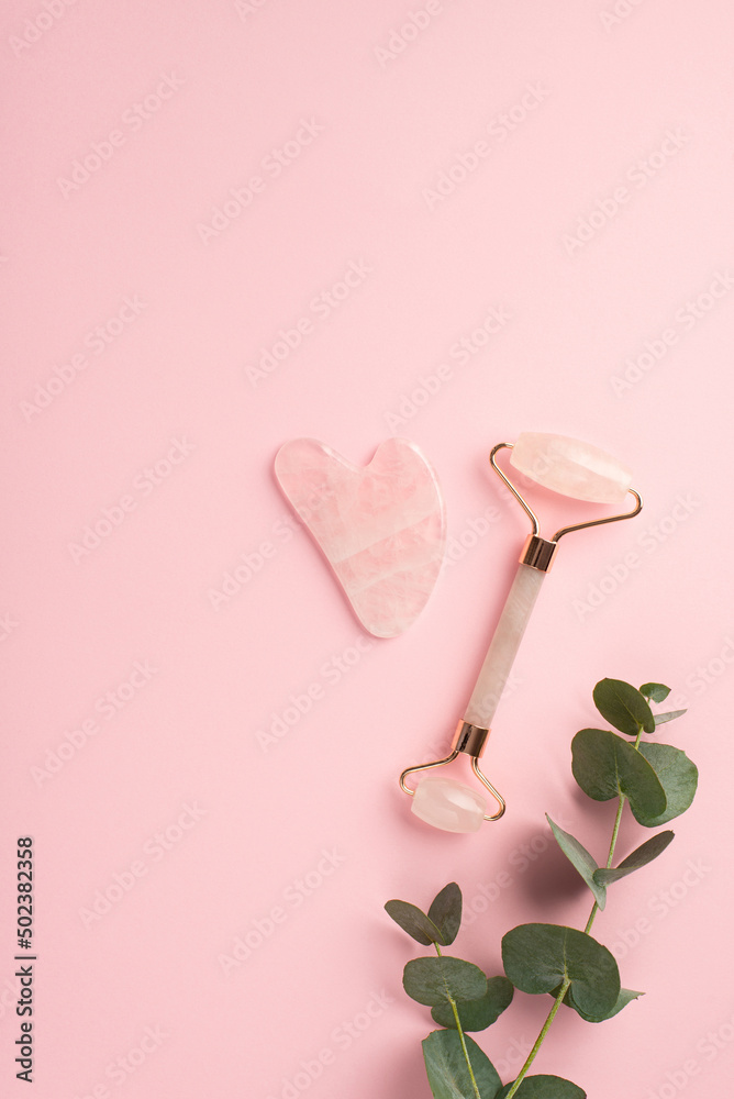 Beauty procedure concept. Top view vertical photo of eucalyptus gua sha and rose quartz roller on isolated pastel pink background with copyspace Beauty procedure concept. Top view vertical photo of eucalyptus gua sha and rose quartz roller on isolated pastel pink background with copyspace