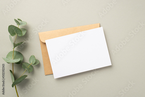 Business concept. Top view photo of paper card craft paper envelope and eucalyptus sprig on pastel grey background with blank space