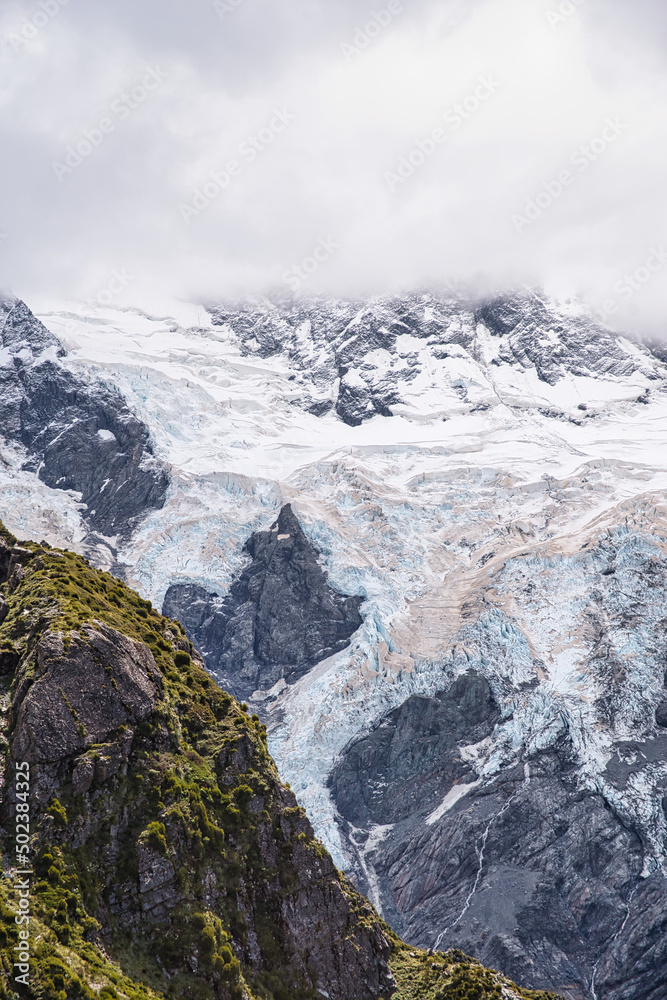 Abstract multi layered image of a mountain covered in snow and ice with dense clouds above and some green in the foreground creating a perfect outdoor advertisement background. Abstract multi layered image of a mountain covered in snow and ice with dense clouds above and some green in the foreground creating a perfect outdoor advertisement background.