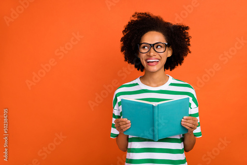 Portrait of attractive cheerful wavy-haired girl reading book copy space solution advert isolated over bright orange color background