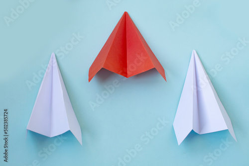a red paper airplane and two white ones on a blue background. The concept of leadership  teamwork and courage.