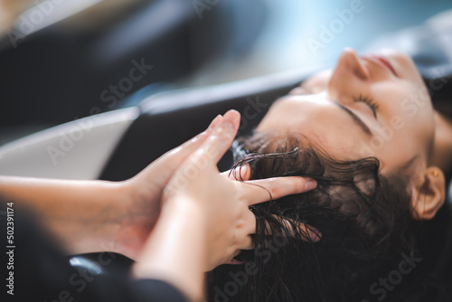 young beautiful woman client getting hair treatment in beauty salon with professional female stylist hairdresser, using shampoo and water on person head to clean and coiffure hair fashion service