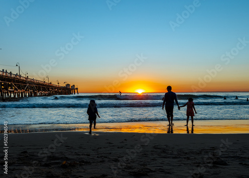 Silhouette of two kids and an adult enjoying late sunset walks at the seashore photo