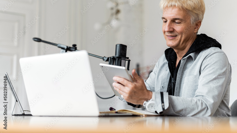 An adult gray-haired man working on the radio blogger uses a laptop and microphone. An adult gray-haired man working on the radio blogger uses a laptop and microphone.