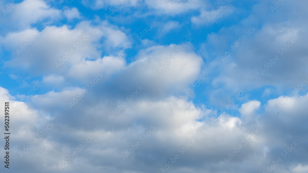 Naklejka premium Blue sky background with clouds. White cumulus clouds in blue sky. Cloudy weather, cloudscape, copy space. Space for text.