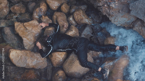 Aerial top view of the almost drowned man lying on the stony sea shore and breathing. Stock. Barely alive man lying on his stomach on big stones, SOS concept.