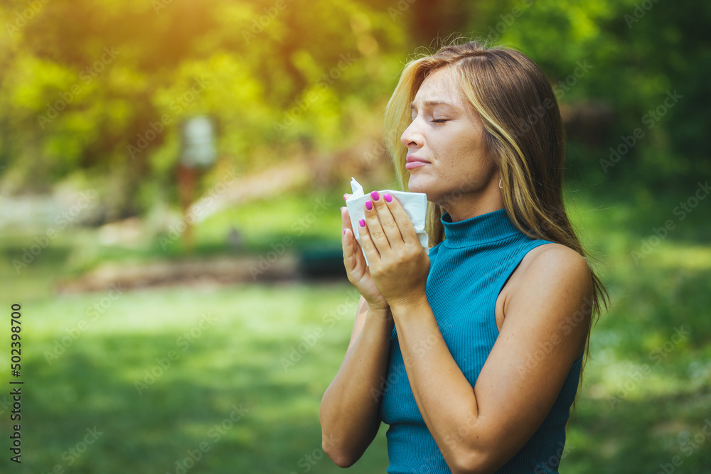 Outdoor shot of displeased Caucasian woman feels allergy, holds white tissuue, stands near tree with blossom, feels unwell, sneezes all time. People and health problems. Spring time. Blooming Outdoor shot of displeased Caucasian woman feels allergy, holds white tissuue, stands near tree with blossom, feels unwell, sneezes all time. People and health problems. Spring time. Blooming