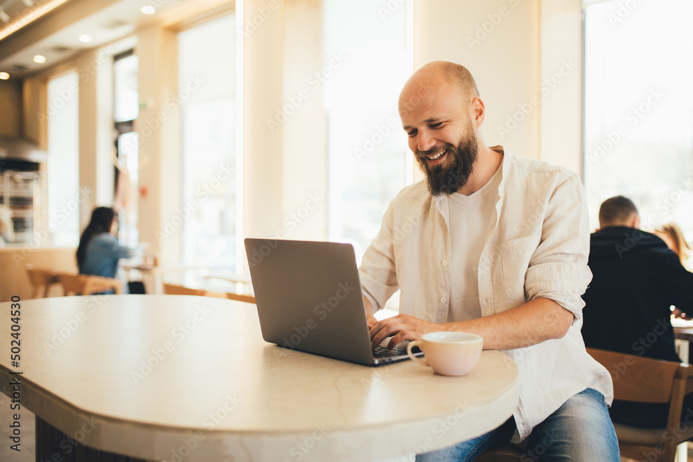 Millennial man working online using his laptop, sitting in a coffee house. Millennial man working online using his laptop, sitting in a coffee house.