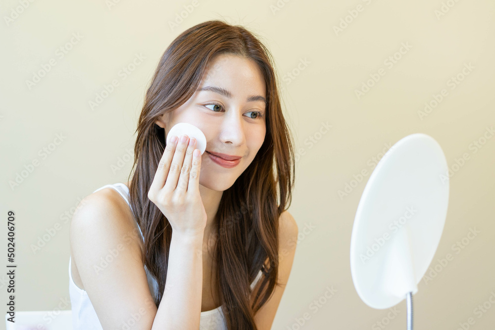 Happy beauty, beautiful asian young woman, girl looking in to mirror, holding cotton pad, applying facial wipe on her face, removing makeup before shower in bathroom, skin care on white background. Happy beauty, beautiful asian young woman, girl looking in to mirror, holding cotton pad, applying facial wipe on her face, removing makeup before shower in bathroom, skin care on white background.