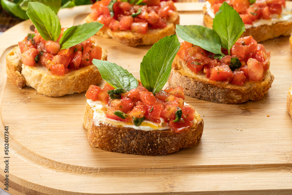 bruschetta with tomato, ricotta and basil, on a wooden board
