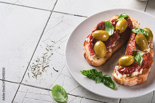 Bruschetta with sun dried tomatoes. Toast or sandwich with ricotta, sun dried tomatoes and Provence herbs with basil servered on a plate on a grey old cracked tile table. Top view banner menu recipe. photo