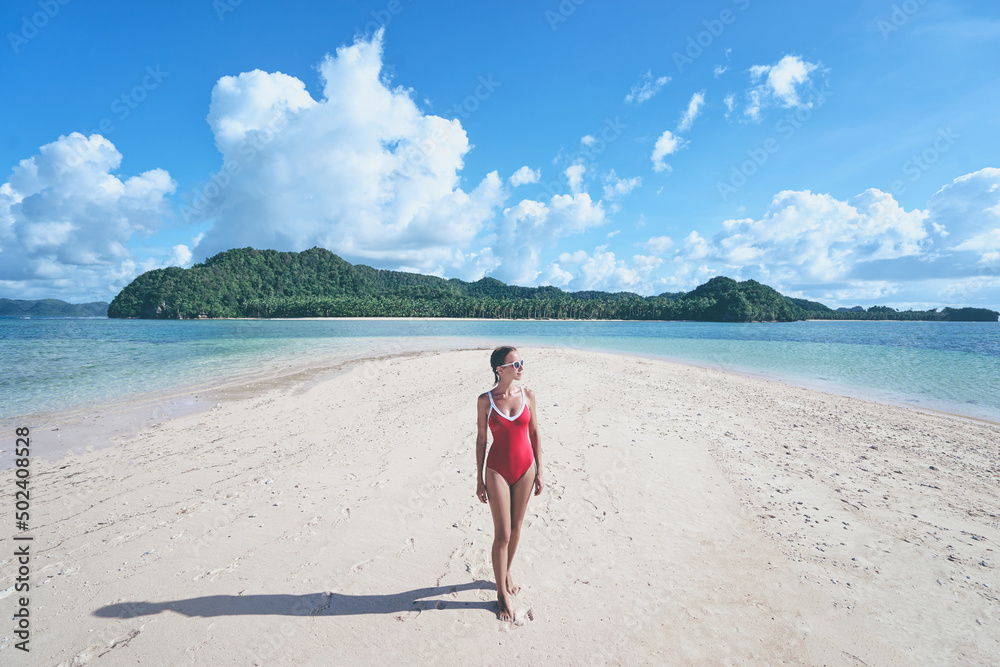 Vacation on the seashore. Young woman in red swimsuit walking on the beautiful tropical white sand beach. Vacation on the seashore. Young woman in red swimsuit walking on the beautiful tropical white sand beach.